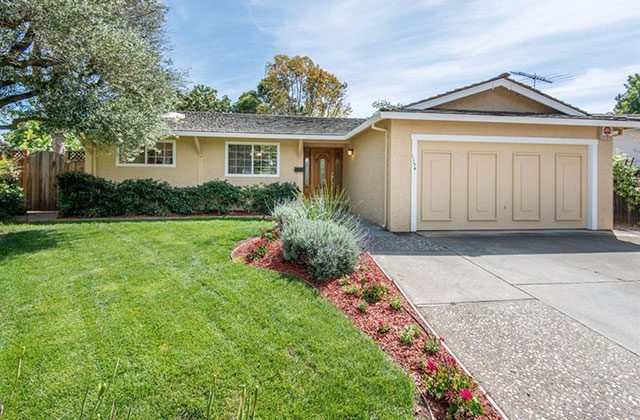 A house with grass and flowers in front of it.