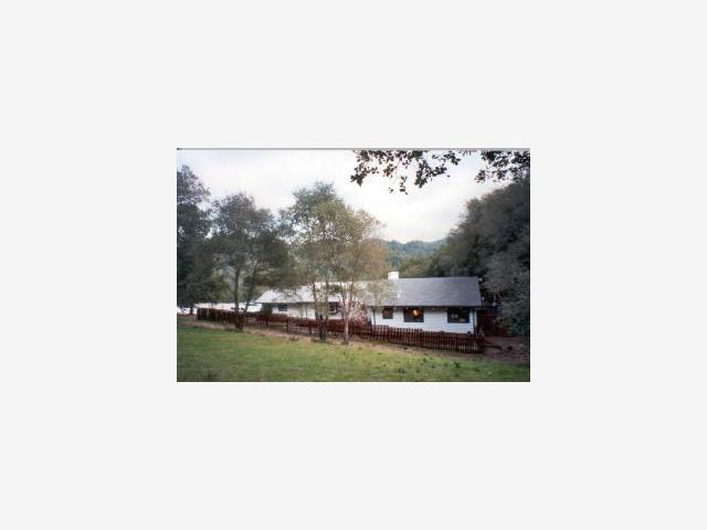 A white house with black roof in the middle of a field.