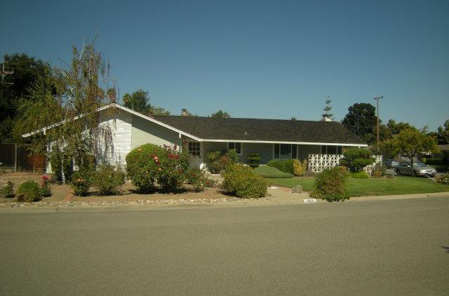 A white house with bushes and trees in front of it.