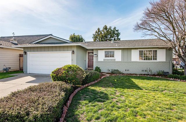 A house with a driveway and bushes in front of it