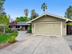 A tan garage door and driveway with palm trees.