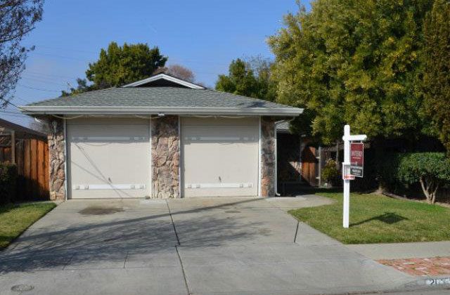 A house with two garage doors and a sign in front of it.