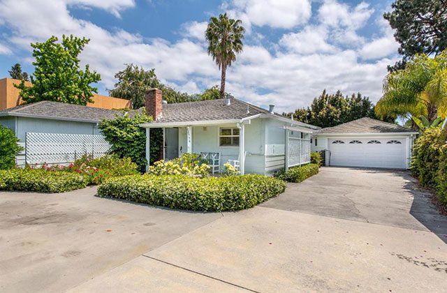 A house with a driveway and bushes in front of it.