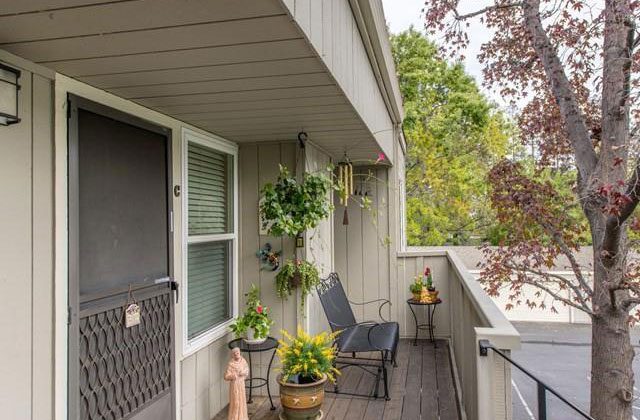 A porch with two chairs and plants on the side.